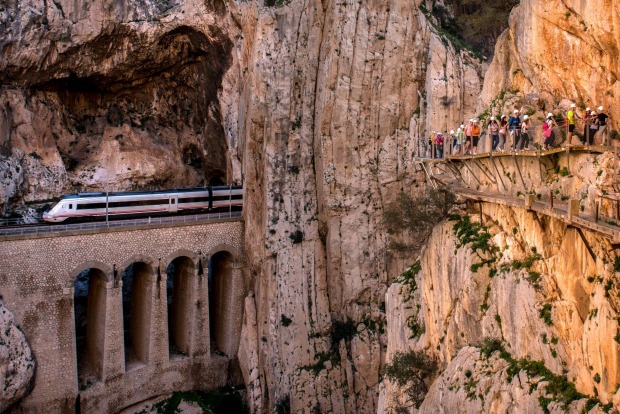 A train passes through a tunnel as tourists walk along the 'El Caminito del Rey' (King's Little Path) footpath in ...